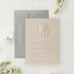 May include: A beige wedding invitation with a debossed sand dollar design. The invitation includes the names Charlotte Sedna and Roman Bennett, the wedding date August 25, 2029, and the location Naples, Florida. A gray envelope is behind the invitation.