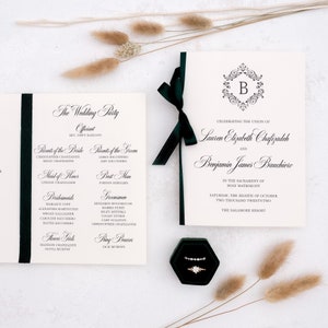 May include: A wedding invitation with a black and white design. The invitation features a monogram with the letter "B" in a decorative frame. The text reads "Celebrating the union of Lauren Elizabeth Chafizadeh and Benjamin James Bauchiero" and includes the date and location of the wedding.