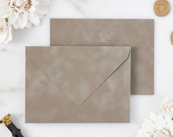 May include: Two taupe-colored envelopes with a textured finish are displayed. The envelopes are positioned on a white surface, with a floral arrangement and gold wax seals. The text "PAPER & LACE" is visible.