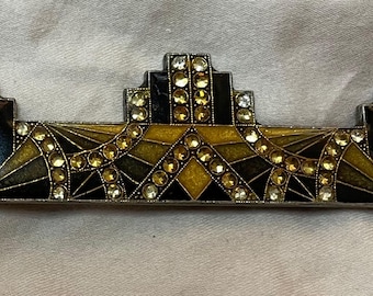 Könnte beinhalten: Art Deco Brosche mit geometrischem Design. Die Brosche hat schwarze, goldene und klare Strasssteine. Die rechteckige Brosche ist etwa 7.6 cm lang und hat einen silberfarbenen Metallrahmen.