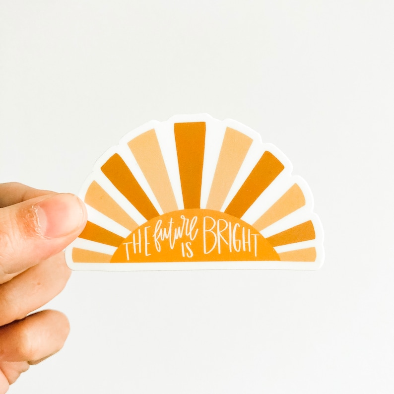 Op de afbeelding: Een sticker met een geel en oranje zonnestralenontwerp en de tekst "The future is bright".