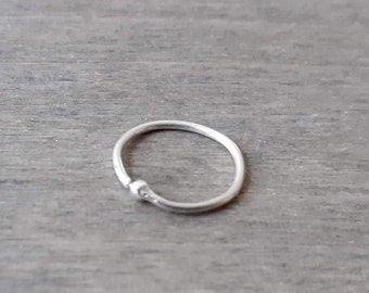 May include: A silver nose ring with a small bead on the side.