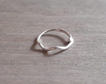 May include: A silver ring with a unique, organic shape. The ring has a smooth, polished finish and a slightly irregular, wavy design. The ring is shown on a neutral, wooden surface.