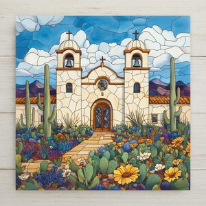 May include: A square wall art print featuring a stained glass style illustration of a mission church with two bell towers, each topped with a cross. Tall saguaro cacti and blooming yellow flowers frame a stone path leading to the arched entrance.