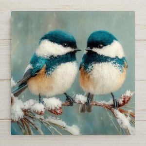 May include: Two small birds with dark blue caps, white faces, and light brown underbellies perched on a snow-covered pine branch. The birds have black beaks and dark eyes, set against a soft, light blue background with falling snow.