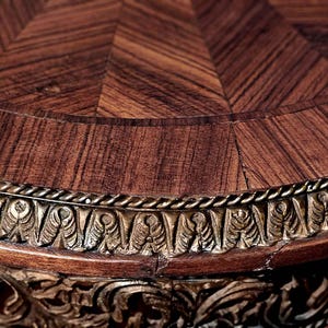 Puede incluir: Una tapa de mesa redonda de madera con un patr&oacute;n decorativo de marqueter&iacute;a y un borde dorado. La tapa de la mesa es de madera oscura con un color marr&oacute;n intenso.