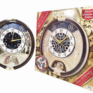 May include: A round Seiko wall clock with a dark brown frame, white dial, and gold hands. The clock features a mechanical gear design, blue crystals, and a small stage at the bottom. It is packaged in a box labelled Special Collector's Edition.