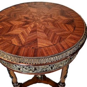Puede incluir: Una mesa redonda de madera con una tapa de marqueter&iacute;a y una base de metal dorado. La mesa tiene un dise&ntilde;o decorativo alrededor del borde de la tapa.