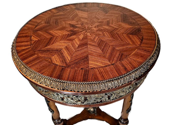Puede incluir: Una mesa redonda de madera con una tapa de marqueter&iacute;a y una base de metal dorado. La mesa tiene un dise&ntilde;o decorativo alrededor del borde de la tapa.