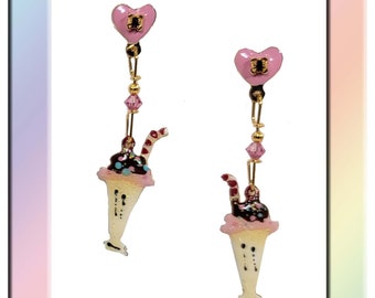 Puede incluir: Un par de pendientes colgantes con un dije de corazón rosa, una cuenta de cristal y un cono de helado esmaltado detallado con chocolate y chispas. Los pendientes son de color dorado.