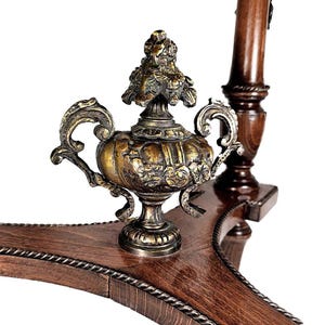 Puede incluir: Una mesa de madera con un remate decorativo de lat&oacute;n en el centro. La mesa tiene un acabado marr&oacute;n oscuro y detalles intrincados.