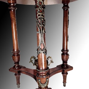 Puede incluir: Una mesa redonda de madera con un borde decorativo de lat&oacute;n alrededor del borde superior. La mesa tiene tres patas con adornos de lat&oacute;n ornamentados y un acabado de madera oscura.