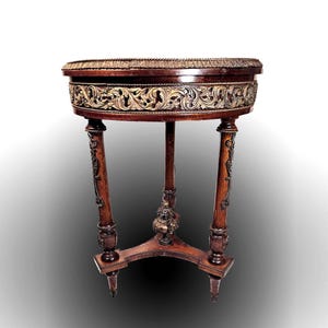 Puede incluir: Una mesa redonda de madera con una tapa tallada pintada de oro y tres patas. La mesa tiene un dise&ntilde;o decorativo y ornamentado.