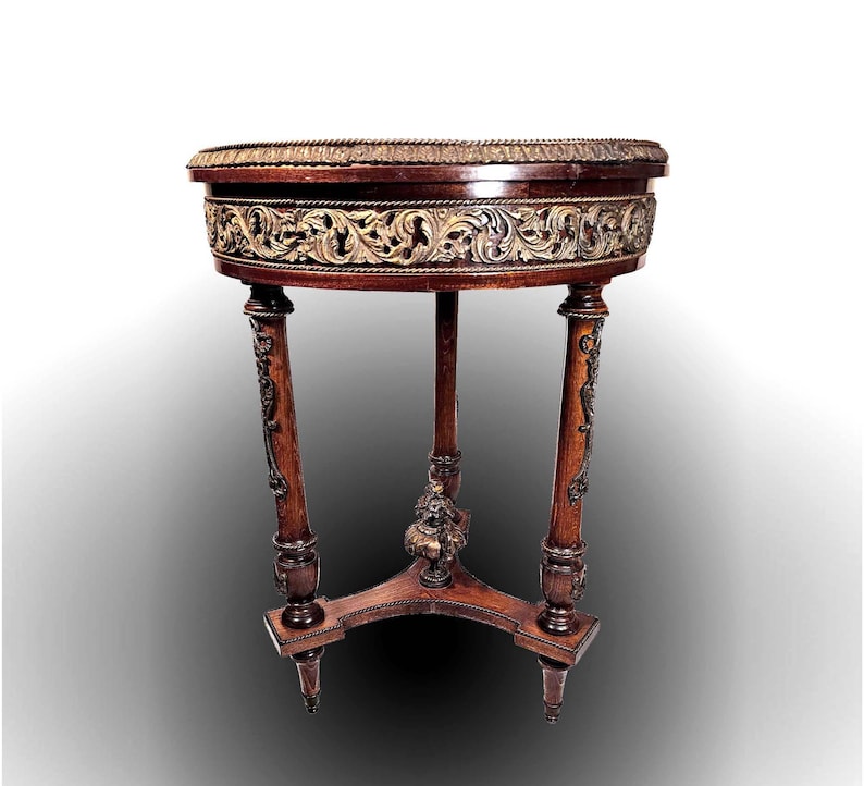 Puede incluir: Una mesa redonda de madera con una tapa tallada pintada de oro y tres patas. La mesa tiene un dise&ntilde;o decorativo y ornamentado.