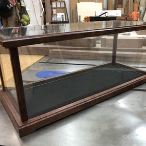 May include: A rectangular wooden display case with a glass top and sides. The case has a black felt lining and a dark wood finish.