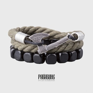 May include: A green rope bracelet with a black and silver axe charm. The bracelet is layered with a black wooden bead bracelet. The bracelet is from the brand "Pakabone Stylish Accessories".