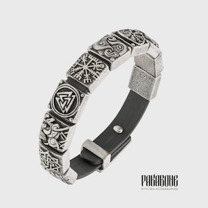 Pode incluir: Uma pulseira de prata com uma tira de couro preto e v&aacute;rios pingentes quadrados com s&iacute;mbolos n&oacute;rdicos. Os pingentes incluem um Vegvisir, um Valknut e um Triskelion. A pulseira tem uma fivela de prata.