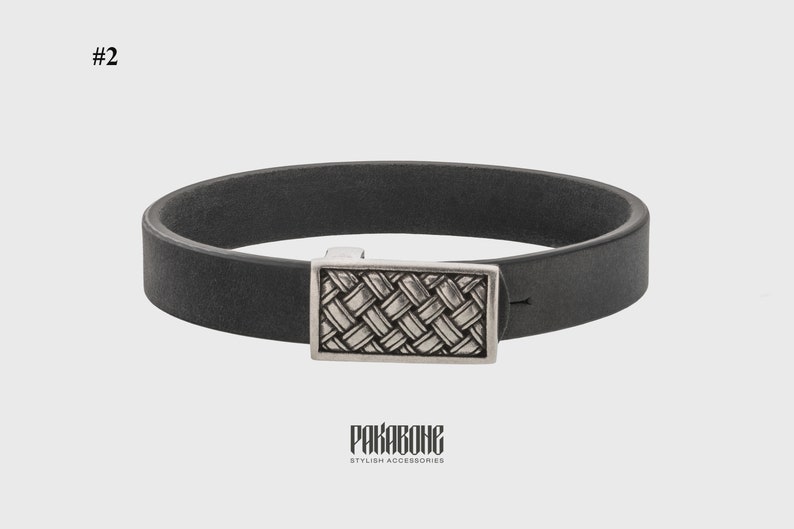 Pode incluir: Um bracelete de couro preto com um fecho prateado com um padr&atilde;o tecido. O bracelete &eacute; etiquetado como "PAKABONE STYLISH ACCESSORIES".