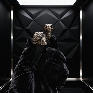 May include: A detailed silver-colored turtle figurine with intricate shell and face details. The turtle is held against a black background, showcasing its design. The figurine is a decorative item.