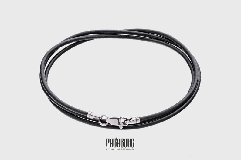 Puede incluir: Un collar de cuero negro con un cierre plateado. El collar est&aacute; hecho de dos hebras de cuero.
