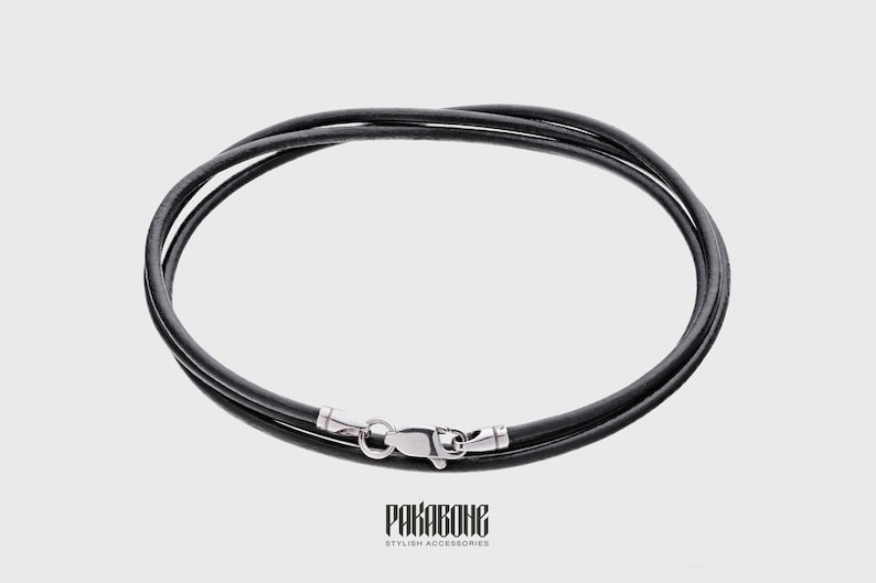 Peut inclure: Un collier en cordon de cuir noir avec un fermoir argent&eacute;.