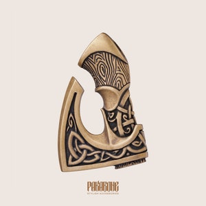 Peut inclure: Une t&ecirc;te de hache dor&eacute;e avec un motif de n&oelig;ud celtique noir. La t&ecirc;te de hache pr&eacute;sente un motif de grain de bois sur le dessus. Le texte "PAKARBONE STYLISH ACCESSORIES" est en bas de l'image.