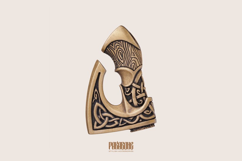 Peut inclure: Une t&ecirc;te de hache dor&eacute;e avec un motif de n&oelig;ud celtique noir. La t&ecirc;te de hache pr&eacute;sente un motif de grain de bois sur le dessus. Le texte "PAKARBONE STYLISH ACCESSORIES" est en bas de l'image.