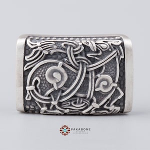 May include: Silver pendant with a detailed, intricate design of a knotwork pattern. The pendant is rectangular and has a textured surface.