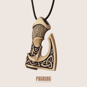 Peut inclure: Un collier avec un pendentif en forme de hache orn&eacute; de n&oelig;uds complexes. La hache est de couleur dor&eacute;e et est suspendue &agrave; un cordon noir.