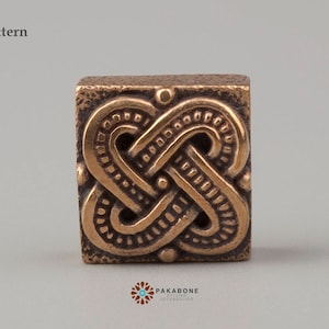 May include: A bronze square tile with an intricate knotwork pattern. The tile has a textured surface and a dark brown color.