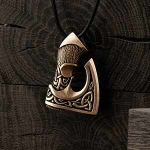 Peut inclure: Un pendentif en bronze en forme de hache avec des motifs complexes de n&oelig;uds celtiques. Le pendentif est suspendu &agrave; un cordon noir.