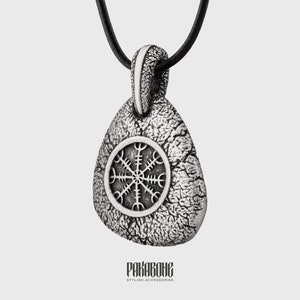 May include: A silver pendant necklace with a black cord. The pendant has a textured surface and a circular design in the centre. The pendant is teardrop-shaped. The brand name "PAKABONG" is at the bottom.