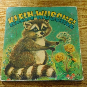 May include: A vintage children's book cover featuring a cartoon raccoon with a green, blue, and yellow background. The title of the book is "KLEIN-WUSCHEL".