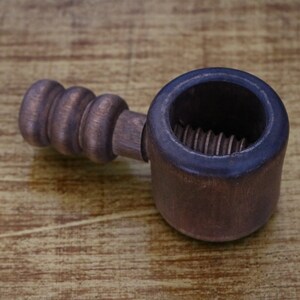 Puede incluir: Un cascanueces de madera con un acabado marrón. El cascanueces tiene un mecanismo de tornillo roscado y un mango con una perilla redonda.