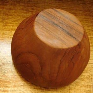 May include: A wooden bowl with a natural brown finish. The bowl is made from a single piece of wood and has a smooth, rounded shape.