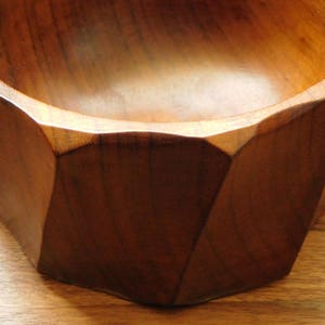 May include: A wooden bowl with a geometric, octagonal shape. The bowl is made of dark brown wood and has a smooth, polished finish.