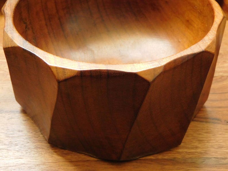 May include: A wooden bowl with a geometric, octagonal shape. The bowl is made of dark brown wood and has a smooth, polished finish.