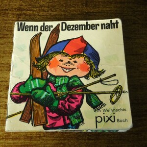 May include: A vintage children's book cover featuring a cartoon illustration of a child wearing a blue and red hat, holding skis and ski poles. The book title is "Wenn der Dezember naht" and the text "Ein Weihnachts pixi Buch" is at the bottom.