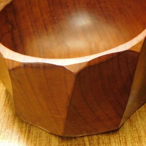 May include: A wooden bowl with a geometric shape and a dark brown color. The bowl is made of a single piece of wood and has a smooth, polished finish.