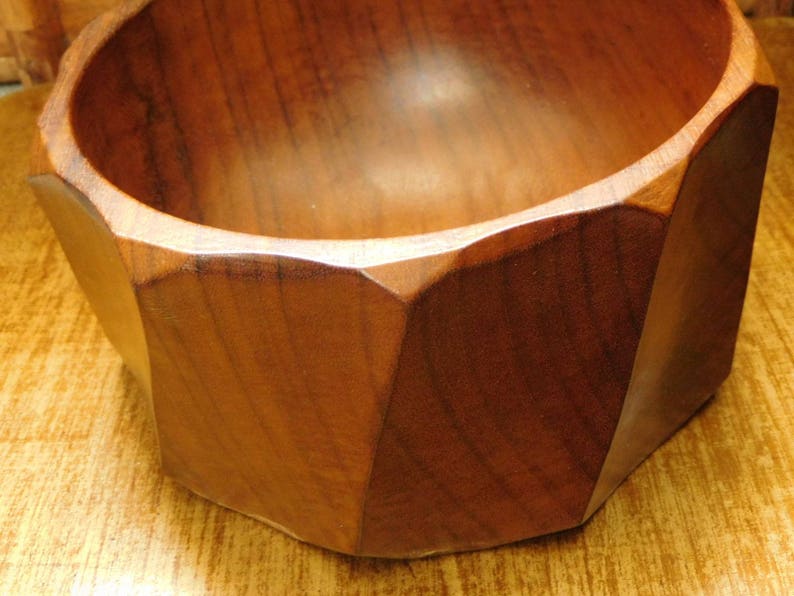 May include: A wooden bowl with a geometric shape and a dark brown color. The bowl is made of a single piece of wood and has a smooth, polished finish.