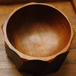 May include: A wooden bowl with a dark brown finish and a geometric shape. The bowl has a smooth, polished surface and is empty.