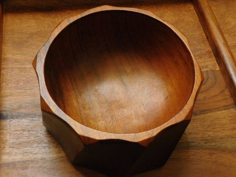 May include: A wooden bowl with a dark brown finish and a geometric shape. The bowl has a smooth, polished surface and is empty.