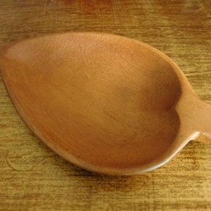 Könnte beinhalten: Eine kleine, hölzerne Servierplatte in Form eines Blattes. Die Platte ist aus hellbraunem Holz gefertigt und hat eine glatte, polierte Oberfläche.