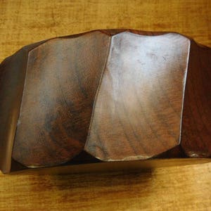 May include: A dark brown wooden bowl with a unique, faceted design. The bowl is made of a smooth, polished wood and has a natural, rustic look.