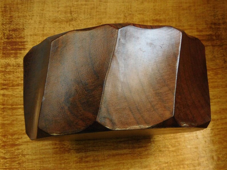 May include: A dark brown wooden bowl with a unique, faceted design. The bowl is made of a smooth, polished wood and has a natural, rustic look.
