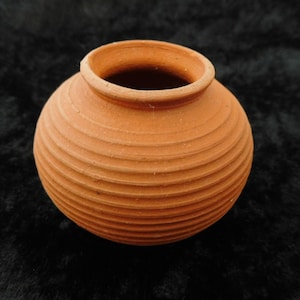 Könnte beinhalten: Ein kleiner, runder Terrakotta-Topf mit geripptem Design. Der Topf ist hellbraun und hat eine glatte, unglasierte Oberfläche.