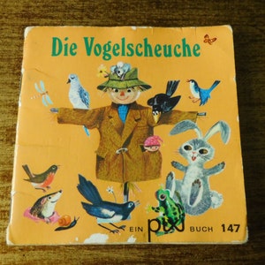 May include: A vintage children's book cover, titled "Die Vogelscheuche" in green, featuring a scarecrow illustration. The cover includes various birds and animals, such as a rabbit and a frog, set against a yellow backdrop. The book is marked "Ein pix BUCH 147".