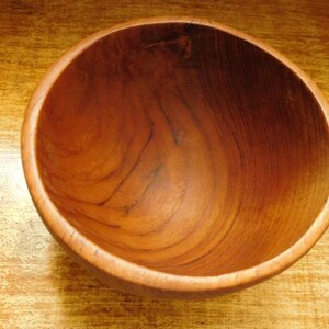 May include: A large, round wooden bowl with a natural wood finish. The bowl is empty and has a smooth, polished surface.