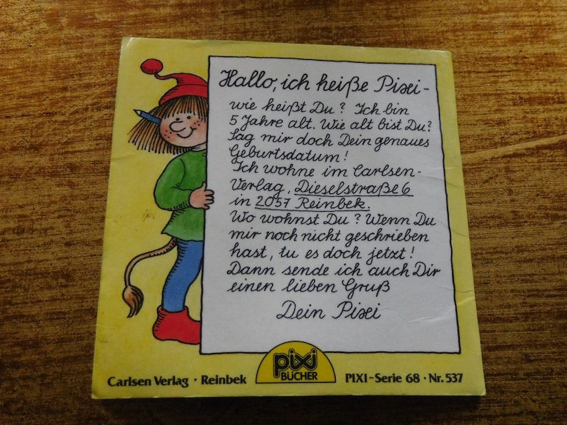 Puede incluir: Una portada de libro ilustrada en amarillo y rojo con un personaje de dibujos animados que sostiene un cartel que dice "Hallo, ich hei&szlig;e Pixi - wie hei&szlig;t Du?" El libro se titula "Pixi-Serie 68 - Nr. 537" y es publicado por Carlsen Verlag, Reinbek.