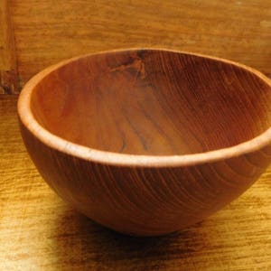 May include: A wooden bowl with a natural brown finish. The bowl is made of wood with a grain pattern.